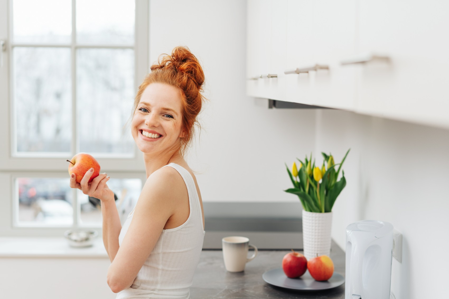 ragazza-in-cucina-sorridente-che-mangia-una-mela